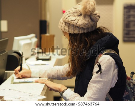 women wearing wool hats standing beside and holding a pen in right hand writing at reception Royalty-Free Stock Photo #587463764