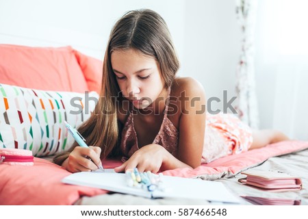 10-12 years old pre teen girl writing diary in pink bedroom