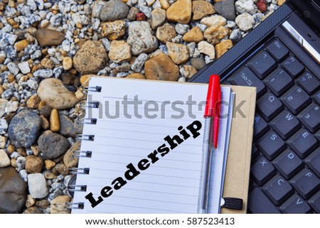 Notebook,red pen and laptop on stone floor background.  Top view written  with Leadership.