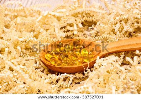 Vitamin D capsules in a wooden spoon on a wooden background, fish oil softgels, health and diet concept 