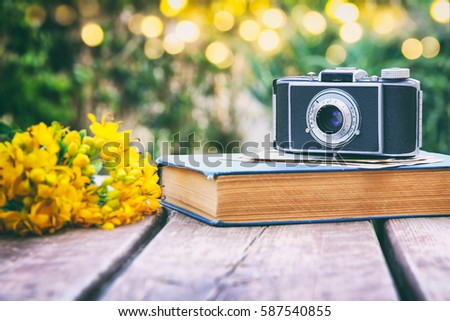 old book, vintage photo camera next to field flowers on wooden table outdoors at afternoon. selective focus