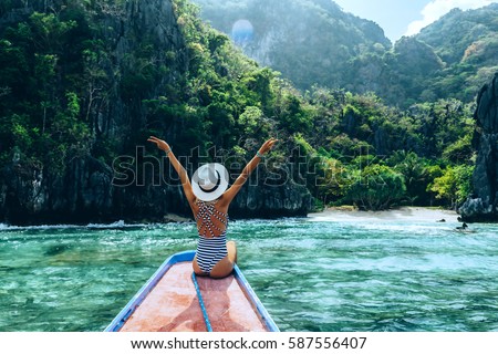Back view of the young woman in hat relaxing on the boat and looking at the island. Travelling tour in Asia: El Nido, Palawan, Philippines. Royalty-Free Stock Photo #587556407