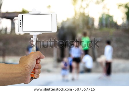 Smartphone on a selfie stick on zoo background. Blank screen with copy space