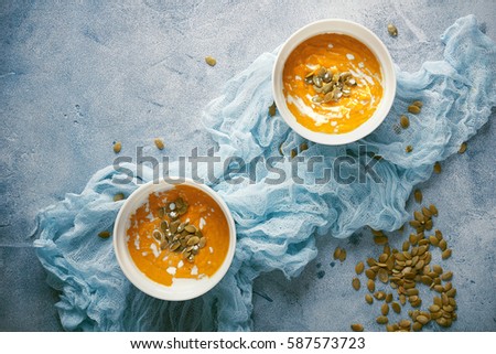 Pumpkin soup with seeds and cream in a white bowl in a wooden box on a blue background, Selective focus, Top view, Copy Space