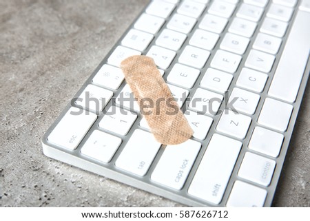 Computer keyboard with adhesive bandage on grey table