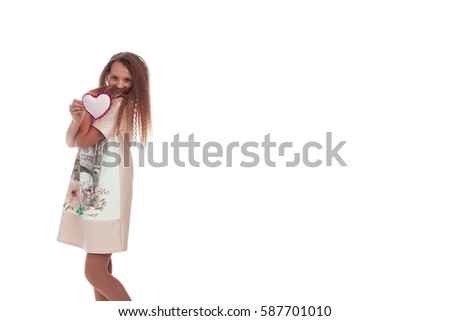 Sweet girl with long hair in a pink dress with a soft toy heart in the hands posing on a white background in studio