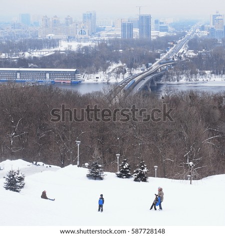KIEV - UKRAINE - FEBRUARY 2017: Mother with children playing on the snow-covered hill in Kiev on the backdrop of a winter city. Children sledding. Concept: childhood. happy