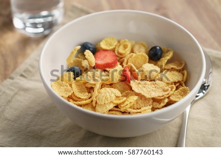 berries falling into corn flakes for breakfast in bowl on table, breakfast preparation