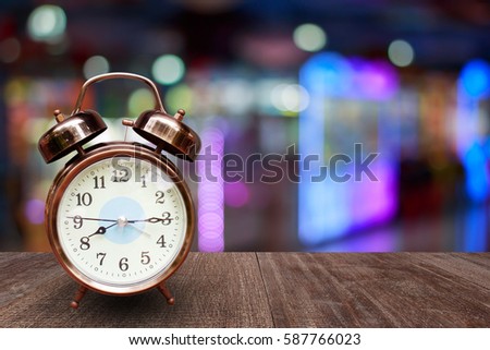 Alarm clock on wood table on screen over blurred in shopping mall background