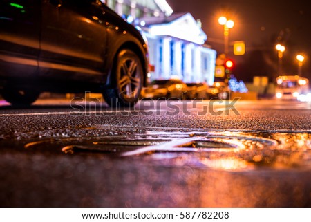 Rainy night in the big city, the car rides near the illuminated luxurious mansion. Close up view of a hatch at the level of the asphalt