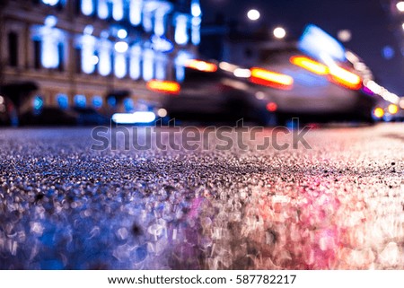 Rainy night in the big city, the road with driving cars. Close up view from the asphalt level, image in the blue tones