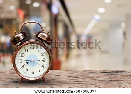 Alarm clock on wood table over blurred in shopping mall background