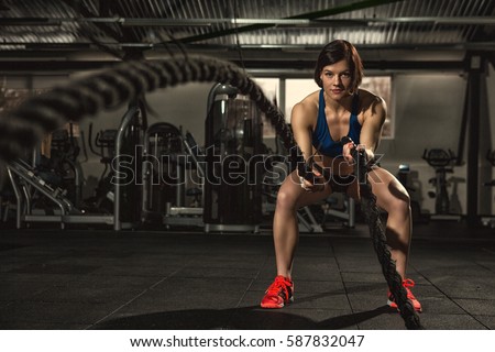 Battle ropes session. Attractive young fit and toned sportswoman working out in functional training gym doing crossfit exercise with battle ropes copyspace battling ropes cross-fit workout motivation Royalty-Free Stock Photo #587832047