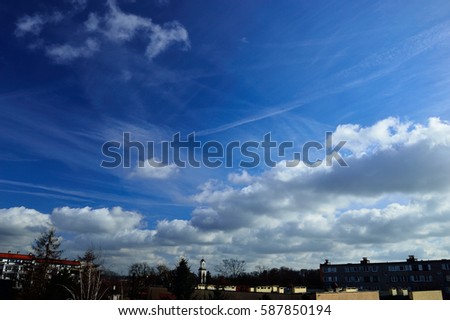 Clouds on a background of blue sky and over the roofs of houses.

