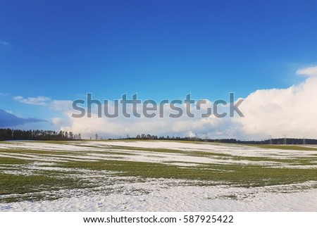 spring landscape in Europe. melting snow, green grass and blue skies with clouds. Royalty-Free Stock Photo #587925422