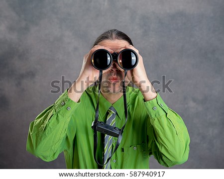 young man in green shirt and necktie looking through a binoculars