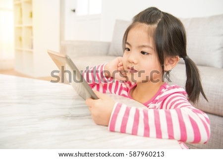 pretty kids girl enjoy watching video cartoon on digital tablet mobile pad at desk in the living room at home. family activity concept.