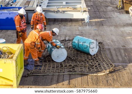 Offshore worker on a construction barge handling a lubricant drum for transfer by crane using a cargo net. 