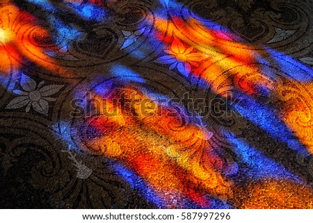 Colorful light spots on the stone mosaic floor. Sunlight through the stained glass window.