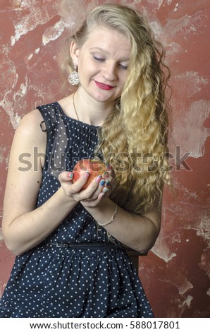 Young blonde girl with curly long hair in a polka-dot dress eating an apple