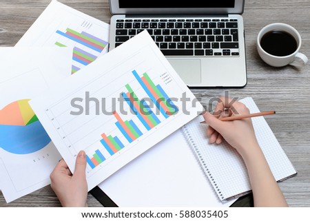 Woman's hands writing in a notepad and holding results of sales depicted on the graphics