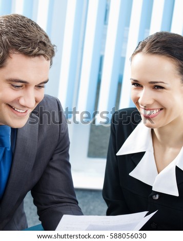 Two young happy smiling businesspeople, or businessman and client working with documents at office. Success in business, partnership and teamwork theme concept. 