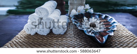 A stack of white towels and a container of water and a flower. Accessories for spa