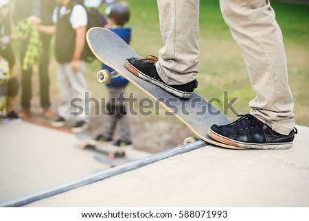 Skater boy stands on big ramp coping in skatepark.Skateboarder guy rides skate board in open outdoor concrete park.Cool extreme summer sports for youth.Focus on sneakers