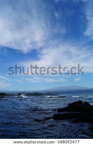 Black Sand Beach, Rocks, Blue Sky, and Clouds with Snow Capped Mountain in Background on the Big Island Hawaii