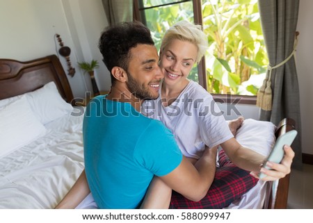 Young Couple Sit On Bed, Take Selfie Photo Happy Smile Hispanic Man And Woman Using Cell Smart Phone, Lovers In Bedroom