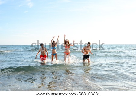 four happy friends young people man and woman having fun at ocean beach jumping together in the sea