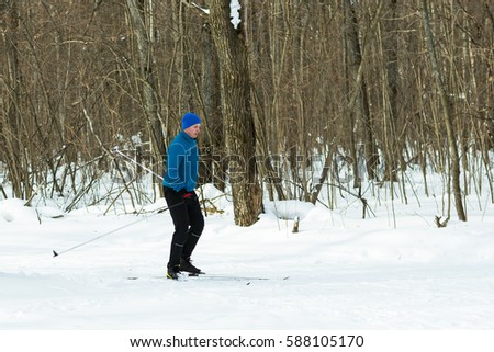 Man in a blue suit runs on skis in the winter woods. Ice ridge course skiing. Healthy lifestyle concept.