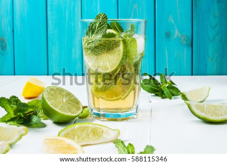 Mojito cocktail with lime and mint in highball glass on a wood table. Blue background.