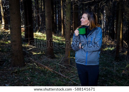 Woman with a green metal cup in her hands in forest trail. Recreation and healthy lifestyle outdoors, autumn woods in mountains, inspirational nature. Fitness and trekking and activity concept.