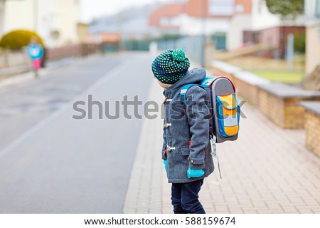 Little kid boy with eye glasses walking from the school. Child on a street. Preschooler wearing warm spring, autumn or winter clothes, glasses and backpack. Happy student or people. Education concept