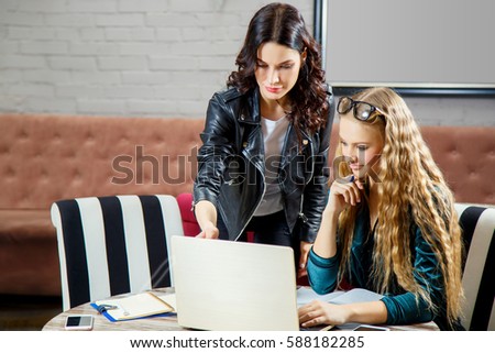 Two beautiful young women working on a laptop and discussing business issues. Two business women discussing a new project in the restaurant. Two girls freelancer working remotely.