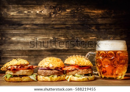 three Burger and mug of beer on wooden background bar