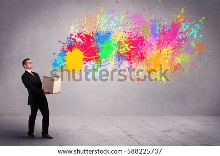A young smiling business male holding a paperboard box with illustration of colourful spray paint splash on urban wall background concept.