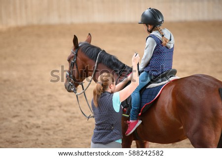 Girl in helmet Learning Horseback Riding. Instructor teaches teen Equestrian. Royalty-Free Stock Photo #588242582