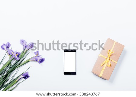 Bouquet of purple irises, mobile phone and gift box on white background, top view