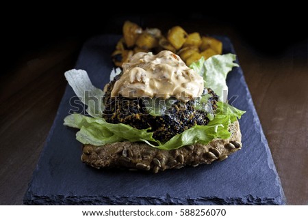 Quinoa Burger on a slate tray with sauce on top accompanied by potatoes
