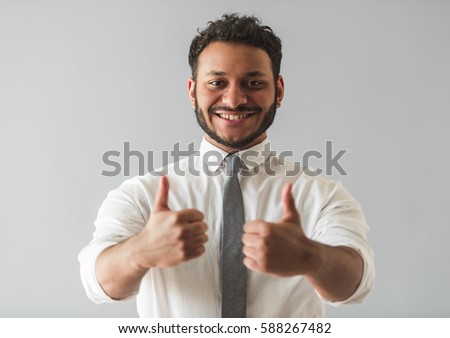 Handsome Afro American businessman in suit is showing thumbs, looking at camera and smiling, on gray background