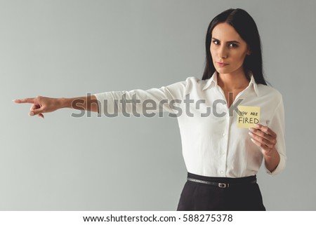 Business woman is holding a note "you are fired" and pointing away, on gray background