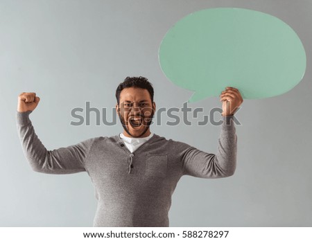Handsome Afro American guy is holding a speech bubble and screaming, on gray background