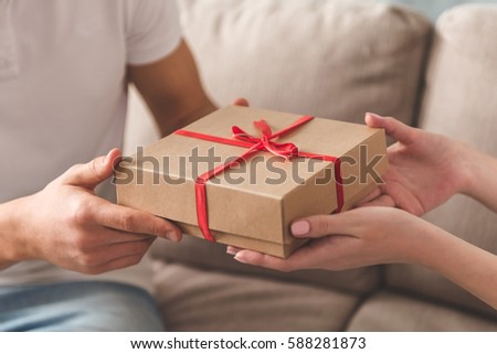 Cropped image of beautiful young couple holding a gift box while sitting on couch at home