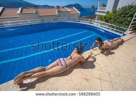 Two women sunbathing on the edge of the pool