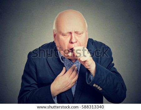Old man coughing holding fist to mouth isolated on gray background Royalty-Free Stock Photo #588313340