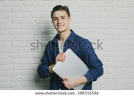 Happy young man with laptop in hands on brick wall
