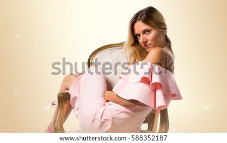 Pretty model woman posing in studio with a pink dress on vintage armchair on ocher background