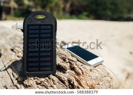 Battery solar energy device on a background of the sandy beach of an uninhabited island. Charge smart phone from the solar battery. Royalty-Free Stock Photo #588388379